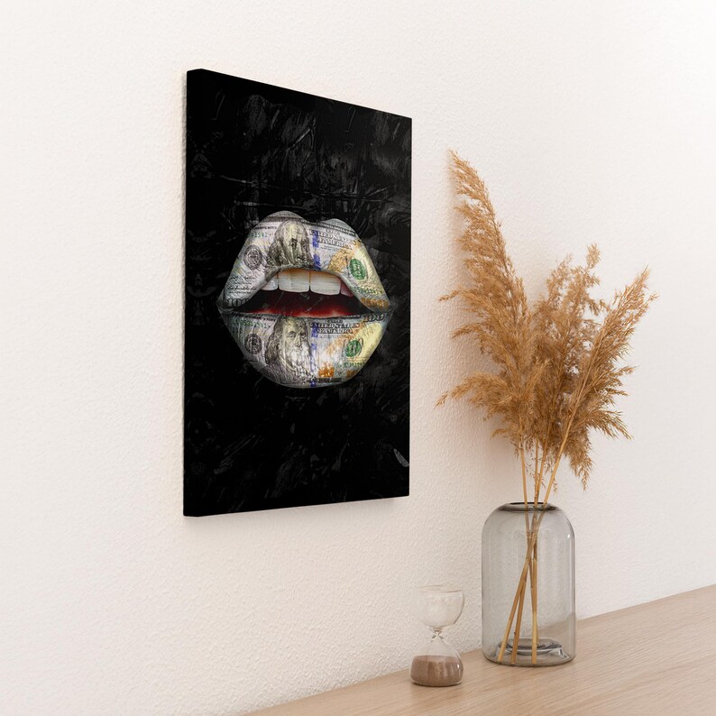 Puede incluir: Impresi&oacute;n en lienzo que muestra unos labios formados por billetes de 100 d&oacute;lares estadounidenses, sobre un fondo negro. Los labios est&aacute;n abiertos, revelando el interior rojo. La obra de arte est&aacute; montada en una pared blanca.