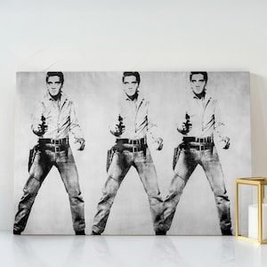 May include: Black and white canvas print featuring a repeated image of a person in a white shirt, jeans, and a gun holster, holding a gun. The artwork has a pop art style and is displayed on a white surface.
