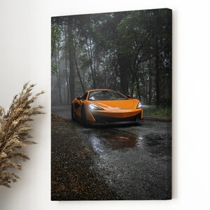 May include: An orange sports car is captured on a wet, winding road surrounded by a forest. The car's sleek design and vibrant color contrast with the muted tones of the natural environment. The image is a canvas print.