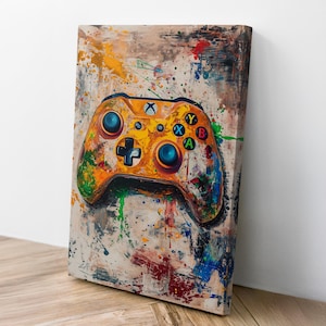 May include: An abstract painting of a yellow Xbox controller with colorful button details. The artwork features a splatter paint effect with various colors, including blue, green, red, and yellow. The canvas is leaning against a white wall.