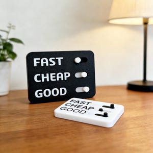 May include: A black and white desk accessory with the words "FAST", "CHEAP", and "GOOD" printed on it. The accessory has three toggle switches and a matching white base with the same text and switches.
