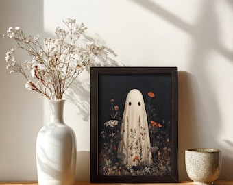 May include: A framed art print featuring a whimsical ghost figure in a field of flowers. The ghost is draped in a white sheet with two black eye holes. The artwork has a dark background with orange and white flowers. A white vase with dried flowers is to the left.