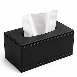 Puede incluir: Una caja rectangular negra para pañuelos con costuras blancas visibles a lo largo de los bordes. La caja presenta una abertura ovalada central en la superficie superior, a través de la cual un pañuelo de papel blanco sobresale hacia arriba.