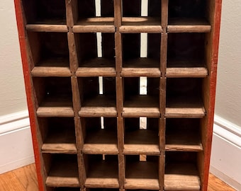 May include: A rectangular wooden storage crate featuring a red exterior frame and a natural wood interior grid with twenty individual compartments. The structure includes metal corner reinforcements at the top and bottom edges for added durability.