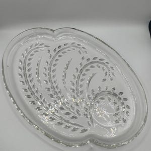 Peut inclure: Plat à servir en verre transparent de forme ovale avec un motif décoratif de feuilles. Le plat a un bord festonné et convient pour servir des entrées ou des desserts. Le motif de feuilles est gravé dans le verre.