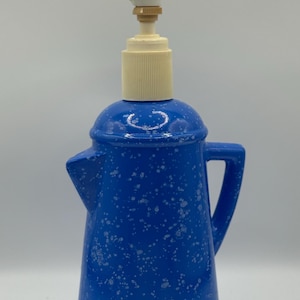 Puede incluir: Dispensador de jabón de cerámica azul con bomba blanca y asa. El dispensador tiene un patrón moteado y tiene forma de cafetera vintage. La bomba es de color blanquecino.