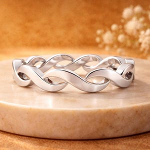 Peut inclure: Une bague argentée présentant un motif métallique torsadé continu en forme d'infini. L'anneau possède une surface polie et réfléchissante avec des maillons incurvés et lisses qui forment un design interconnecté sur toute la circonférence.