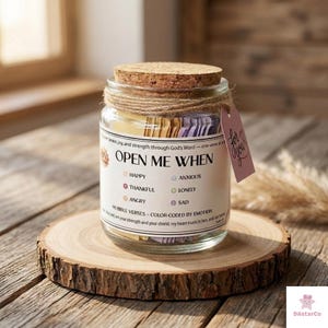 Op de afbeelding: Een glazen pot met een kurken deksel en touw, met het opschrift "Open Me When". De pot bevat kleurgecodeerde Bijbelverzen voor verschillende emoties. Een klein roze label zegt "For You". De pot staat op een houten schijf.