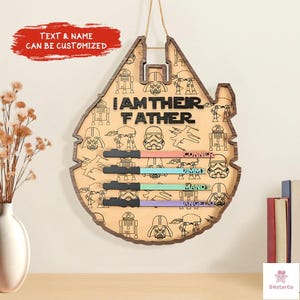 a wooden sign with a Star Wars theme, hanging on a wall. The sign has a Star Wars logo and the text "I AM THEIR FATHER" written on it. There are also various Star Wars characters and elements, such as the Millennium Falcon, Star Wars Death Star, and the Millennium Falcon's tail, which are visible on the sign.