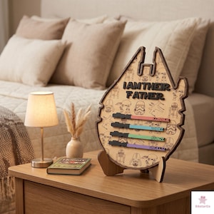 a wooden stand with a Star Wars-themed design, displaying a list of names and a message that says "I AM THEIR FATHER". The stand is placed on a wooden table next to a lamp and a book.