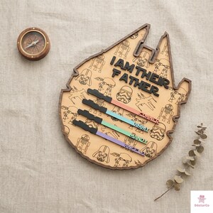 a wooden board with a Star Wars theme, including various characters and a compass. The board has the text "I AM THEIR FATHER" written on it, and there are names below the characters, likely representing family members.