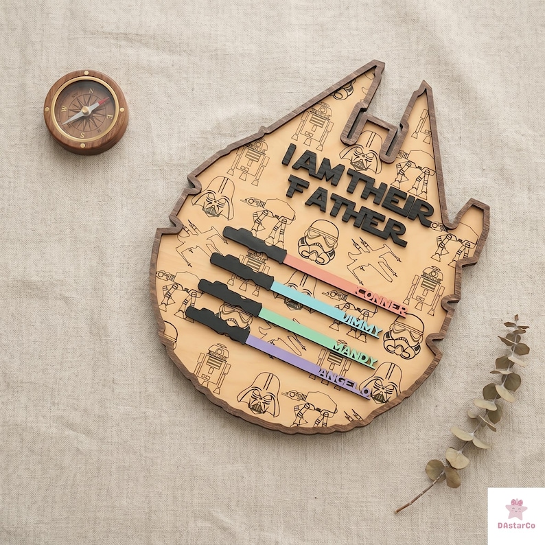 a wooden board with a Star Wars theme, including various characters and a compass. The board has the text "I AM THEIR FATHER" written on it, and there are names below the characters, likely representing family members.