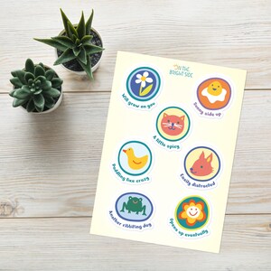 Könnte beinhalten: Ein Aufkleberbogen mit sieben kreisförmigen Designs, bunten Illustrationen und Texten wie Will grow on you, Sunny side up, A little spicy, Paddling like crazy, Easily distracted, Another ribbiting day und Opens up eventually.