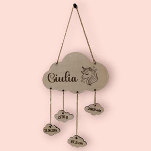 Puede incluir: Adorno de pared de madera con forma de nube con el nombre "Giulia" y una ilustración de unicornio. La nube tiene cuatro colgantes más pequeños con forma de nube con la siguiente información: 25.06.2015, 2770 g, 20h31 min y 47,5 cm.