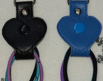 May include: Two hair tie holders with silver clasps. One is black with black, teal, and purple hair ties. The other is blue with black, purple, and teal hair ties. Each holder has a heart-shaped design.