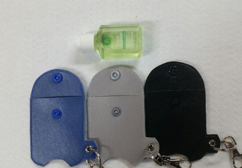 May include: Three different colored leather keychains with snap closures and a metal ring. The keychains are designed to hold a small bottle of hand sanitizer. The keychains are blue, gray, and black.