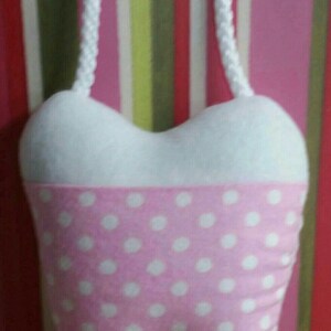 May include: A pink and white tooth-shaped plush toy with white polka dots. The toy is hanging from a white rope.