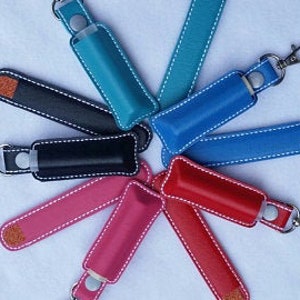 May include: Assortment of colorful leather keychains with a small pocket for a lip balm or other small item. The keychains are available in teal, blue, black, pink, red, and light blue.