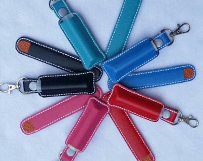 May include: Assortment of colorful leather keychains with a small pocket for a lip balm or other small item. The keychains are available in teal, blue, black, pink, red, and light blue.