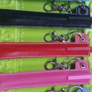 May include: Five keychain pen holders in different colors: black, red, pink, blue, and light blue. Each holder has a silver keychain and a pen with a clear plastic tip.
