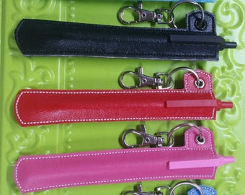 May include: Five keychain pen holders in different colors: black, red, pink, blue, and light blue. Each holder has a silver keychain and a pen with a clear plastic tip.