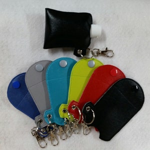 May include: Assortment of seven colorful leather keychains with a small pocket for a hand sanitizer bottle. Each keychain has a silver metal ring and a silver metal clasp. The keychains are in the following colors: blue, gray, teal, yellow, red, black, and black.