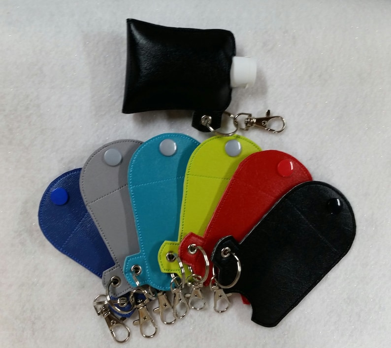 May include: Assortment of seven colorful leather keychains with a small pocket for a hand sanitizer bottle. Each keychain has a silver metal ring and a silver metal clasp. The keychains are in the following colors: blue, gray, teal, yellow, red, black, and black.
