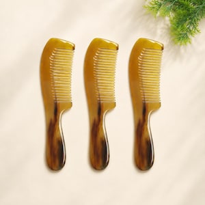 May include: Three hair combs with a smooth, curved handle and a fine-toothed edge. Each comb features a translucent, mottled amber and dark brown pattern throughout the material, creating a distinct, natural-looking appearance for each individual piece.