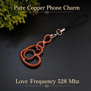 May include: A phone charm made of twisted copper wire forming an infinity-like shape, attached to a black cord with a silver-toned metal clasp. The text Pure Copper Phone Charm and Love Frequency 528 Mhz is displayed in the image.