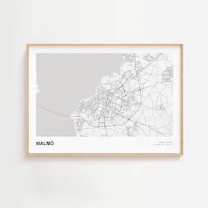May include: A framed print of a map of Malmö, Sweden, in black and white. The city's streets and buildings are detailed. The word "MALMÖ" is printed in bold black letters at the bottom left. The frame is a light wood color.