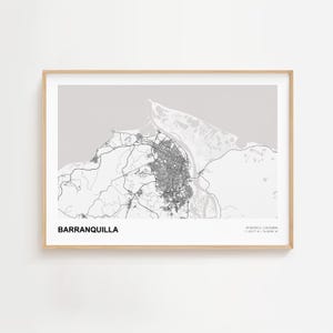 May include: A framed map print of Barranquilla, Colombia, in grayscale. The city's layout is detailed, with roads and buildings depicted. The print includes the city name and coordinates, all within a light wood frame.