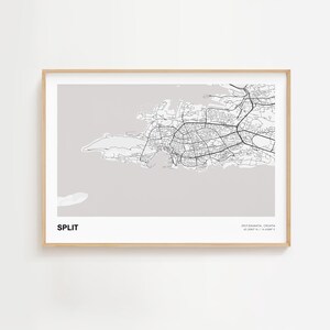 May include: A framed print featuring a detailed black and white map of Split, Croatia, set against a light gray background. The city's name is printed in a bold font at the bottom left, with coordinates at the bottom right.