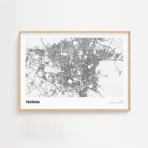 Pode incluir: Uma impressão emoldurada em preto e branco do mapa de Teerão, Irão. O mapa da cidade é detalhado, mostrando ruas e áreas urbanas. A palavra "TEHRAN" é impressa em negrito, com uma fonte sem serifa na parte inferior esquerda. A moldura é de cor de madeira clara.