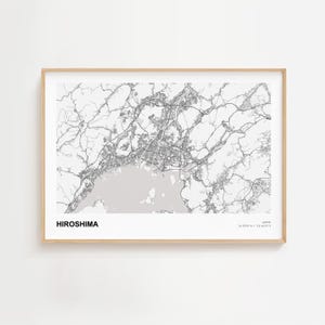 Puede incluir: Impresión enmarcada de un mapa de Hiroshima, Japón, en blanco y negro. El diseño de la ciudad, incluyendo carreteras y vías fluviales, está detallado. La palabra "HIROSHIMA" está impresa en negrita en la parte inferior.