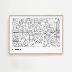 May include: A framed black and white map of El Monte, California, showing a network of streets and geographical features. The map is set against a white background and is enclosed in a light brown wooden frame. The text "EL MONTE" is displayed at the bottom.