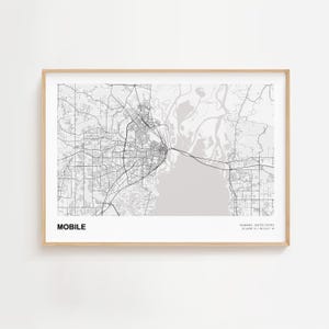 May include: A framed map print of Mobile, Alabama, in black and white. The city's name is printed in a bold font at the bottom left, with the state and coordinates at the bottom right. The map shows roads, waterways, and urban areas.