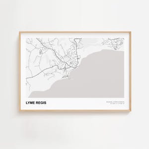 May include: A framed map print of Lyme Regis, England, in black and white. The map shows the town's layout, coastline, and surrounding areas. The print includes the text "LYME REGIS" and coordinates.