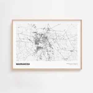 Może przedstawiać: Oprawiona czarno-biała mapa Marrakeszu w Maroku. Mapa przedstawia drogi i budynki miasta. Słowo "MARRAKESH" jest wydrukowane pogrubioną, czarną czcionką w lewym dolnym rogu. Rama jest w jasnym kolorze drewna.