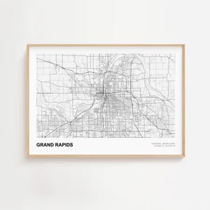 Puede incluir: Una impresión enmarcada en blanco y negro del mapa de Grand Rapids, Michigan, Estados Unidos. El mapa muestra la red de carreteras y vías fluviales de la ciudad. La impresión está en un marco de madera clara.