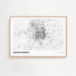 May include: A framed black and white map of Aguascalientes, Mexico. The city map is detailed, showing streets and urban areas. The city name is printed in a bold, sans-serif font at the bottom left. The frame is a light wood color.