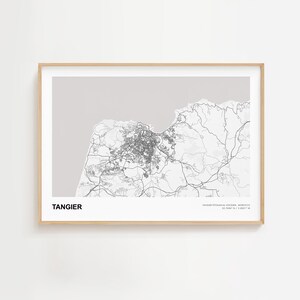 Op de afbeelding: Een ingelijste print met een grijswaardenkaart van Tanger, Marokko. De stadsindeling is gedetailleerd met wegen en gebouwen, tegen een lichtgrijze achtergrond. Het woord "TANGIER" staat onderaan in vette, zwarte letters.