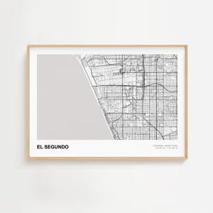 May include: A framed black and white map print of El Segundo, California, with the city name at the bottom. The map shows streets, buildings, and the coastline. The frame is a light wood color.