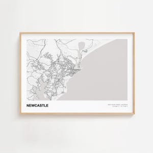 May include: A framed map print of Newcastle, Australia, in black and white. The map shows the city's layout, roads, and coastline against a light gray background. The word "NEWCASTLE" is printed in black at the bottom.