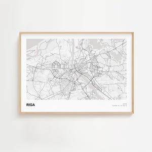 Op de afbeelding: Een ingelijste zwart-wit kaart van Riga, Letland, met de naam van de stad linksonder. De gedetailleerde kaart toont straten en waterwegen. De lijst is licht van kleur.