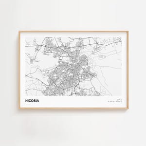 May include: A framed monochrome map of Nicosia, Cyprus, displaying the city's road network and urban structure. The city's name is printed in a bold, sans-serif font at the bottom left. The frame is a light wood colour.