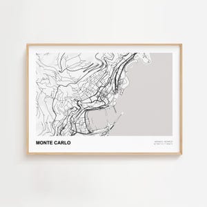 May include: A framed print featuring a detailed black and white map of Monte Carlo, Monaco. The map highlights the city's streets, buildings, and coastline against a light gray background. The words "MONTE CARLO" are printed in bold, black letters.