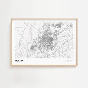May include: A framed monochrome map of Multan, Pakistan. The map details the city's infrastructure, including roads and buildings. The name "MULTAN" is printed in bold, black text at the bottom left. The frame is light-coloured wood.