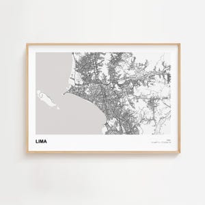 May include: A framed black and white map of Lima, Peru. The map shows the city's layout, including streets and geographical features. The word "LIMA" is printed in white at the bottom left. The frame is made of light-colored wood.