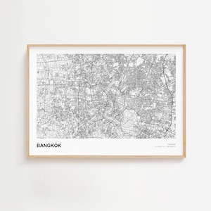 May include: A framed black and white map of Bangkok, Thailand. The map is detailed, showing streets and waterways. The word "BANGKOK" is printed in a bold, white font at the bottom left. The frame is a light wood color.