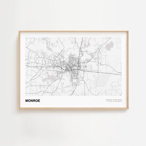 May include: A framed monochrome map print of Monroe, Louisiana, USA. The map details the city's infrastructure, including roads and waterways. The city's name is printed in bold, with the state and coordinates below the map.